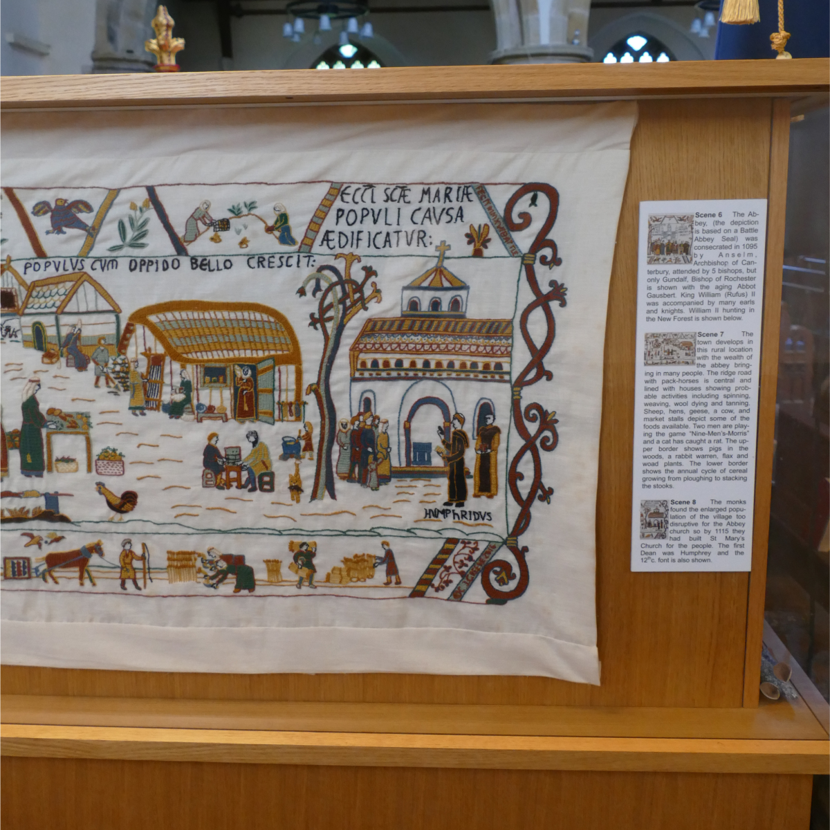 Section of the Battle Tapestry showing medieval scenes of daily life and buildings, embroidered in the style of the Bayeux Tapestry